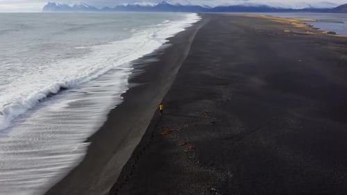 Drone Over Black Sand Beach With Mountain Range In Background