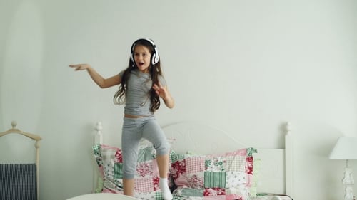 Energetic Girl Dances on Bed with Headphones On