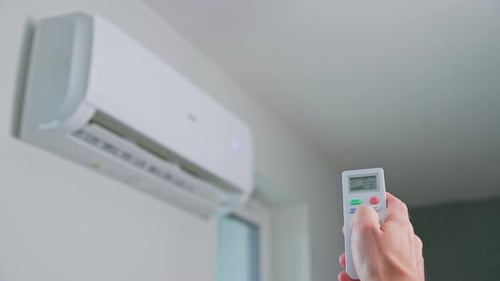 Hand Adjusts Air Conditioner with Remote Control