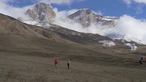 People Hiking Across Grassy Plain in Front of Mountains