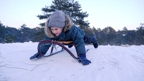 Lächelnder Junge liegt auf Schlittenfahrten vom schneebedeckten Hügel im Winterwald