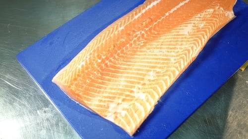 Gloved Cook Cuts Salmon on Blue Cutting Board