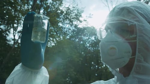 Chemist in Ppe Looking at Flask with Solution Water Analysis From Swamp Wearing Protective Suit and