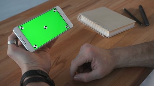 Man Using Phone with Green Screen Display at Desk