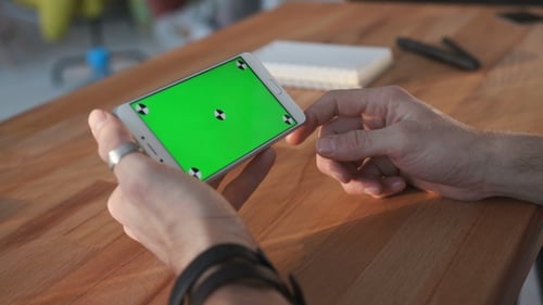 Man Using Smartphone with Green Screen at Table