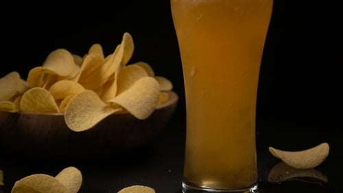 Kartoffelchips werden in eine Holzschale gegossen und Bier wird in ein Glas gegossen