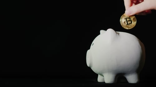 Inserting Bitcoin into Piggy Bank on Black Background