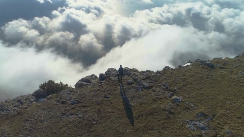 Man Is Standing on the Edge of Mountain Plateau Above the Clouds and Raising Hands