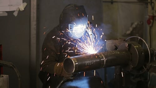 Der funktionierende Schweißer verarbeitet das Metall, bereitet die Basis vor Ein Mann in einem Schutzanzug, Funken.