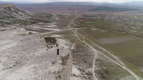 Young Woman with Long Hairs Is Standing at the Edge of White Rock with Raised Hands