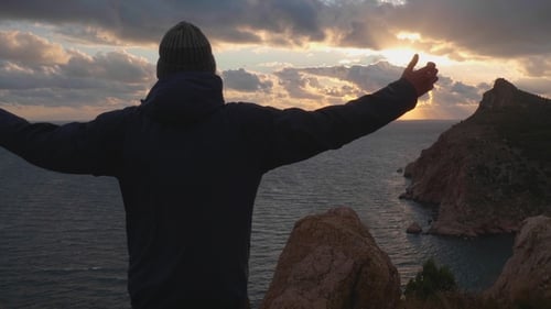 Man Enjoys Coastal Sunrise with Arms Outstretched