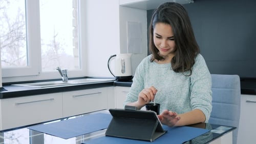 Woman Using Tablet While Stirring Coffee Indoors