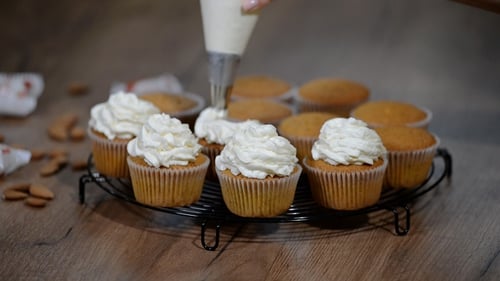 Female Hands Holding Piping Bag Filled with Cream Cheese and Coffee Frosting Decorating Cupcakes.