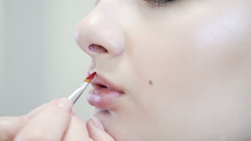 eines attraktiven Schönheitsmädchens beim vollständigen Schminken. Frau trägt rote Lippe
auf