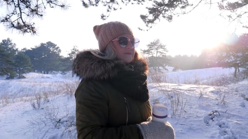 Cute Girl in Sunglasses Holds Cup with Hot Drink in Winter Day Outdoors at Snow Forest