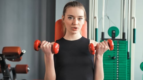 Sporty Young Woman Exercising with Dumbbells in the Gym
