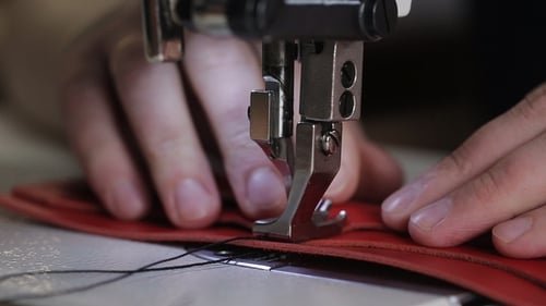 Master Hands verwenden eine Nähmaschine, um Stiche auf einer Lederbrieftasche zu erzeugen