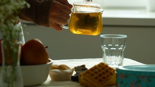 Woman Pours Hot Tea at Breakfast Table