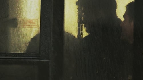 Blurred Silhouettes Waiting in Rainy Bus Station at Night