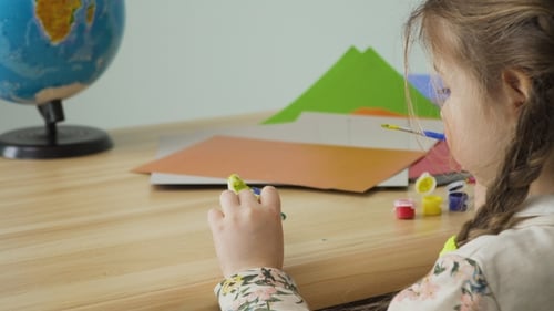 Little Girl with Pigtails Paints Clay Craft Sitting at the Table