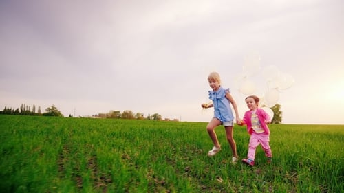 Two Carefree Girls Run Across the Green Meadow, Holding Hands. They Rejoice in the Arrival of Spring