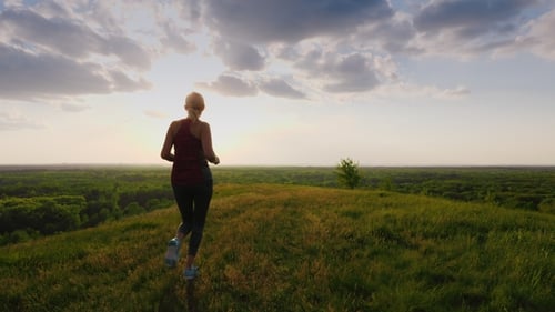 A Run in a Picturesque Place at Sunset. A Woman Runs Towards the Sun, a Back View