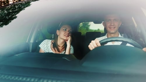 A Young Couple Is Traveling in a Car. View Through the Windshield, It Reflects the Trees and the