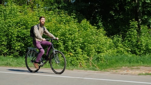 Seitenansicht - Ein junger Mann fährt Fahrrad. Genießt die Reise. Vor dem Hintergrund grüner Bäume in