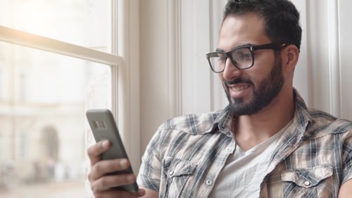 Man Smiling Using Smartphone Indoors Near Window