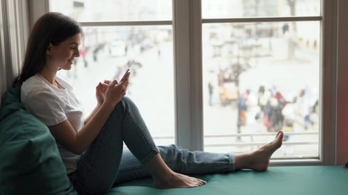 Woman Using Phone in Bright Window Seat