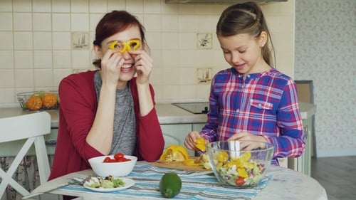 Joyful Mother and Cheerful Daughter Have Fun Grimacing Silly with Vegetables and Looking Into Camera