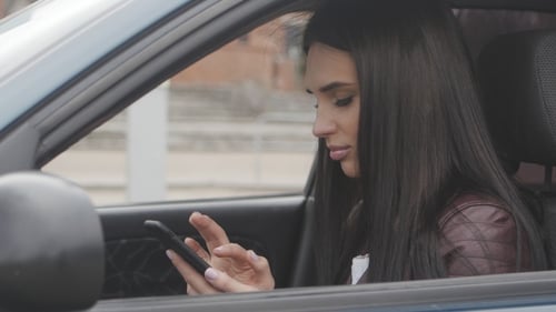Young Woman Uses a Smartphone While Sitting in a Car in the City