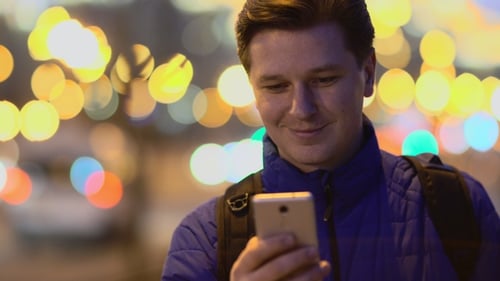 Um jovem usa um telefone celular ao pôr do sol na cidade