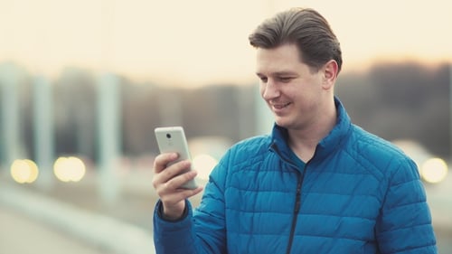 Um jovem usa um telefone celular ao pôr do sol na cidade