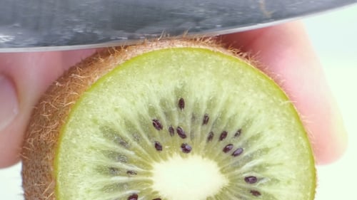 Kiwi Being Sliced in Half on Wet White Background.
