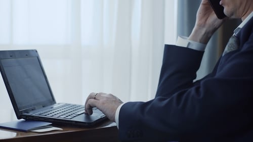 Man in Suit Using Laptop While on Phone