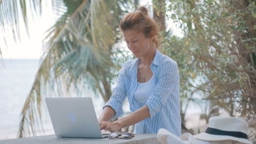 Junge Frau sitzt am Tisch mit einem Laptop mit Blick auf das Meer