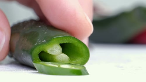 Gehackte grüne Chilis mit Haufen grüner Chilis auf weißem Schneidebrett und weißem Hintergrund
