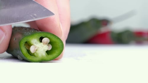 Gehackte grüne Chilis mit Haufen grüner Chilis auf weißem Schneidebrett und weißem Hintergrund