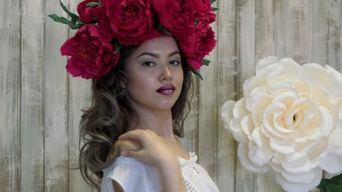 Girl Posing in Front of Camera. Young Woman in a Wreath of Scarlet Peonies on Her Head