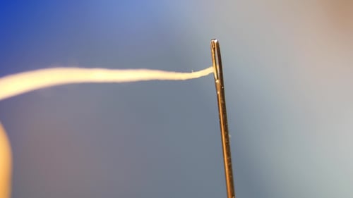 Threading the Eye of a Needle. Pulling the Thread Into the Needle Eye of the Sewing Needle.