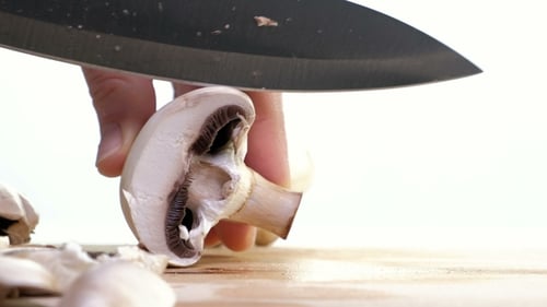 Fresh Mushrooms being Sliced on Wooden Cutting Board