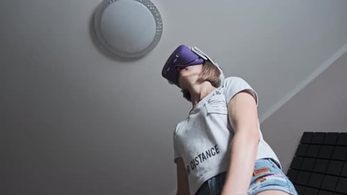 Jovem mulher em um fone de ouvido de realidade virtual joga um jogo em casa