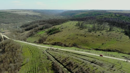 Drone Flies Over Green Hills and Road with Car Fast Driving. Aerial Top View of Country Road