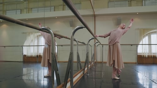 Ballerine en survêtement beige et pointes extensibles sur barre dans la salle de ballet. Femme debout près d'un bar