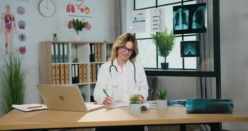 Une femme médecin portant des lunettes et un uniforme d'hôpital travaille avec des rapports papier dans un cabinet médical