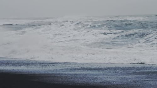 Nebliges Meer stapelt und krachendes Meer am schwarzen Sandstrand