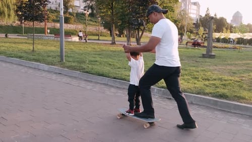 Dad Teaching Son To Drive a Skate in the Summer Park