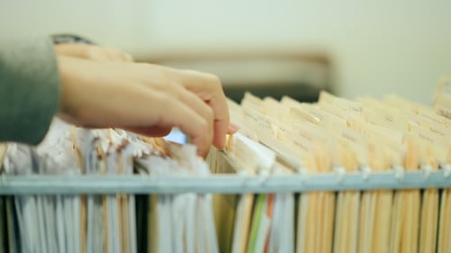 Hands Searching Through Hanging Files in Office Filing Cabinet