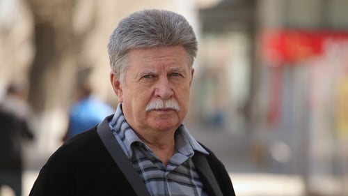 A Serious Old Man with Mustache Puts on Glasses and Stands on an Alley in Spring